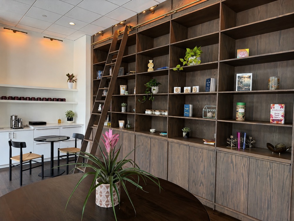 Floor-to-ceiling shelving at the front of Monarch Well, with a rolling ladder, books, teas, candles and the Monarch Well mugs on a shelf behind.